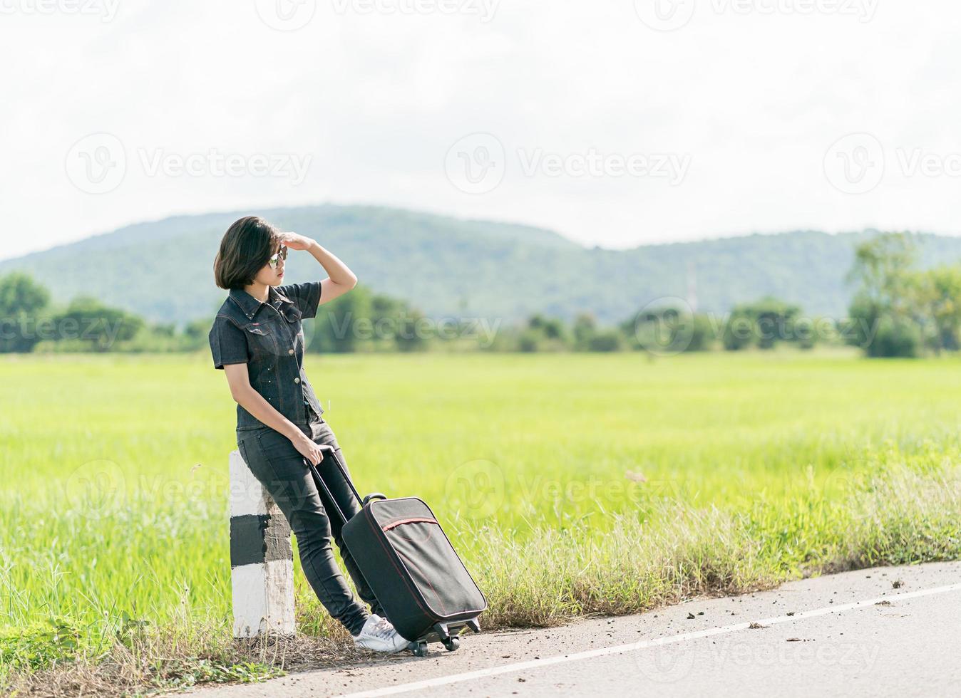 Woman with luggage hitchhiking along a road photo