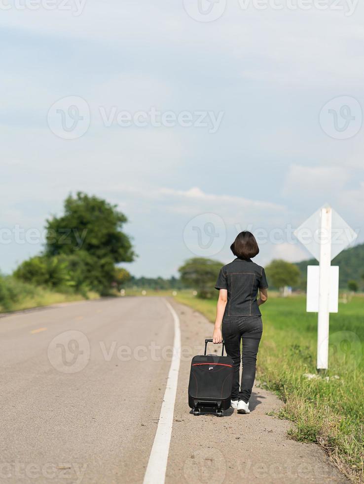 Woman with luggage hitchhiking along a road photo