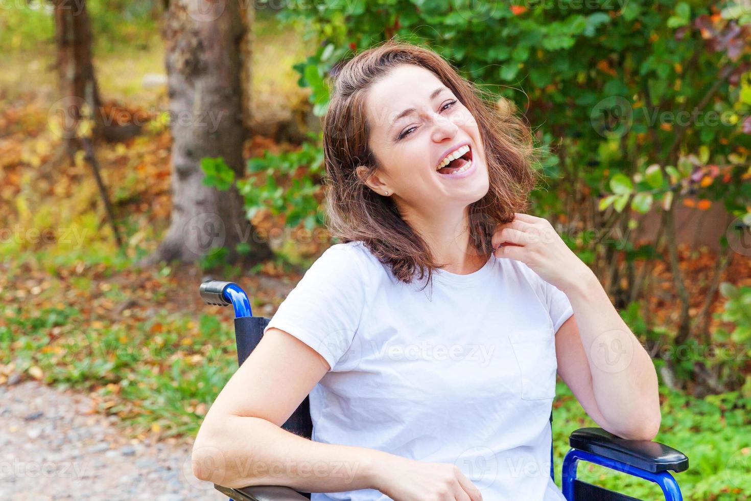 joven discapacitada feliz en silla de ruedas en la carretera en el parque del hospital disfrutando de la libertad. niña paralizada en silla inválida para personas discapacitadas al aire libre en la naturaleza. concepto de rehabilitación. foto