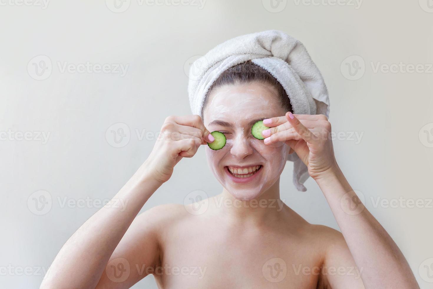 Girl with white facial mask holding cucumber slices isolated on white background. Woman applying white nourishing mask or creme on face. Skin care treatment spa natural beauty and cosmetology concept. photo