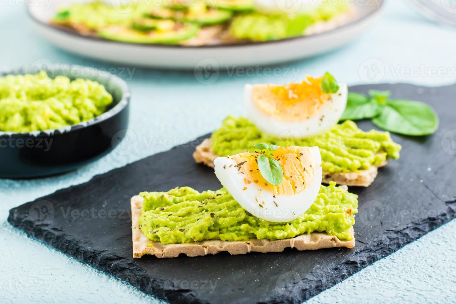 Appetizing sandwiches of crispy bread with avocado and boiled egg on slate. photo