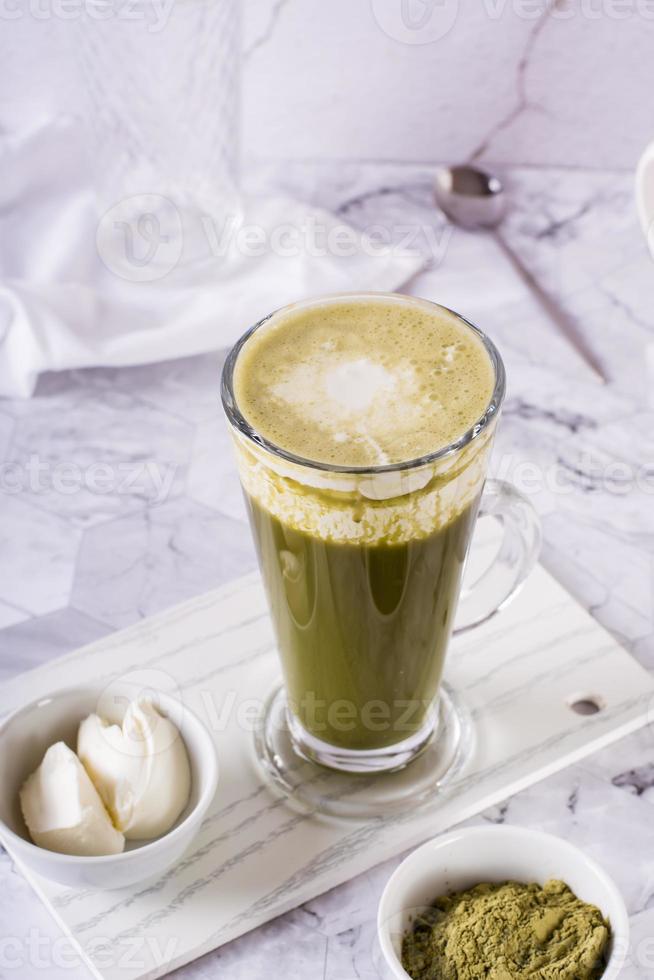 Green matcha ice tea with cream cheese in a glass on the table. Trendy homemade drink. Vertical view photo