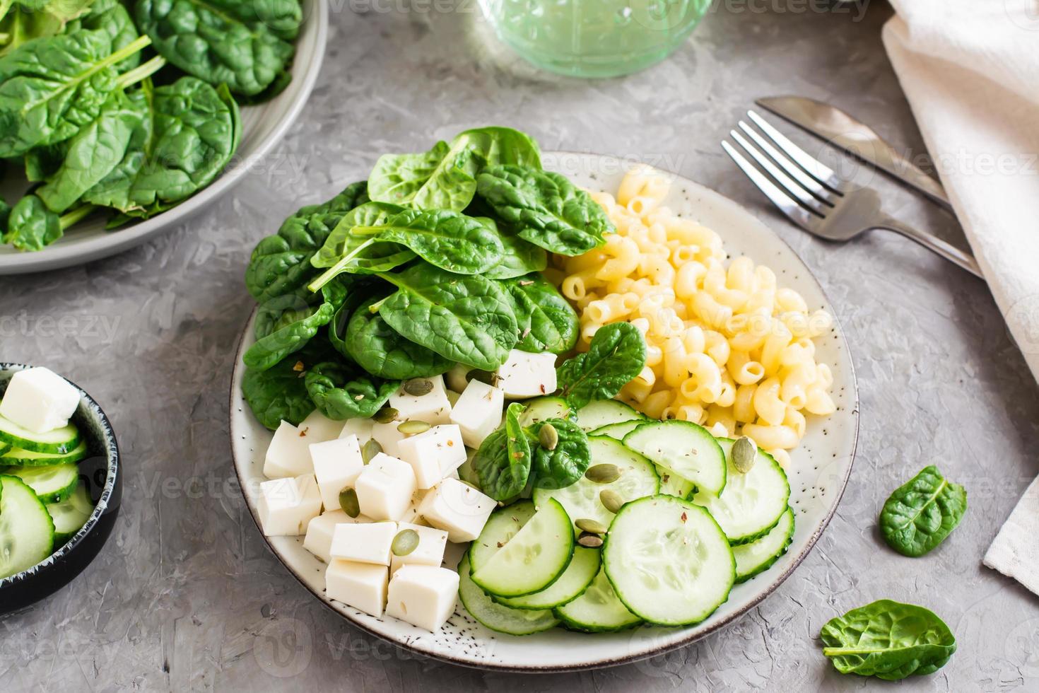 Bowl with pasta, cucumber, cheese and spinach on the table. Healthy vitamin nutrition. Close-up photo