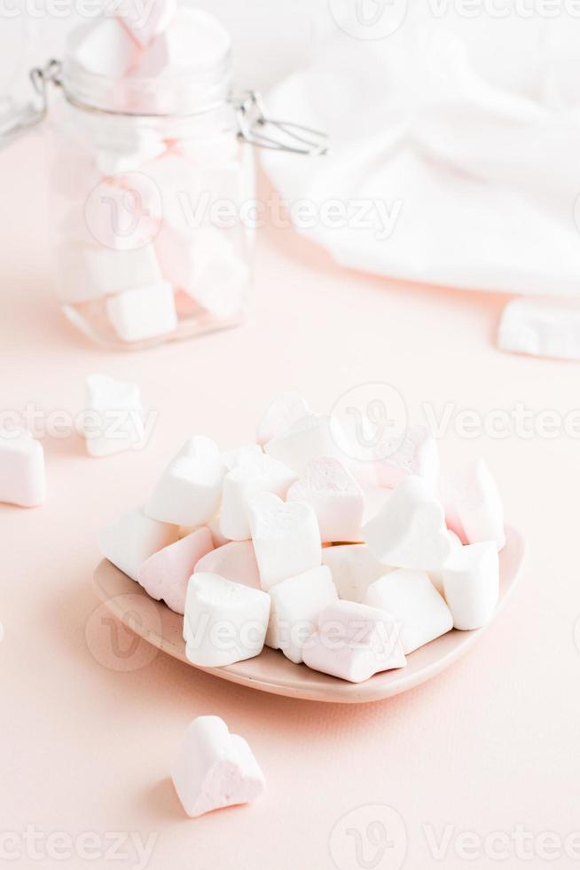 White and pink heart-shaped marshmallows on a saucer on a pink background. Vertical view photo