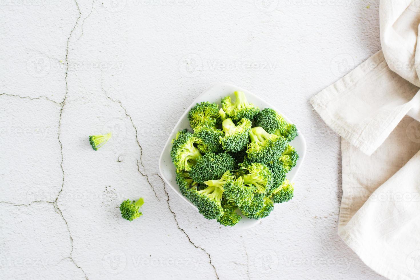 Pieces of raw broccoli on a plate on a light table. Top view photo