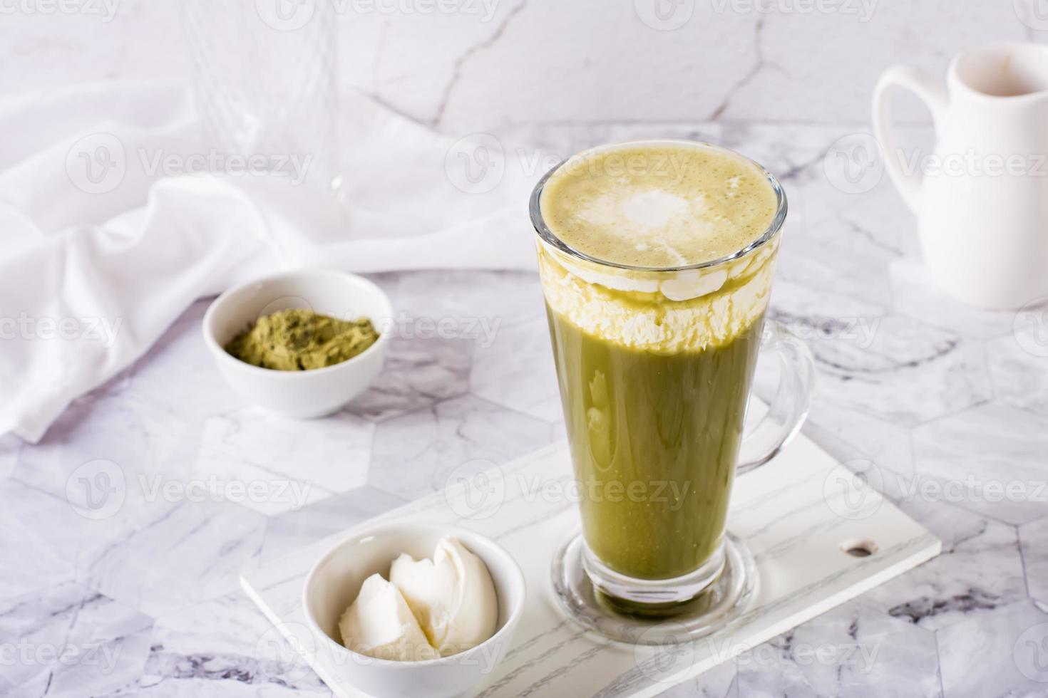 Green matcha ice tea with cream cheese in a glass on the table. Trendy homemade drink. photo