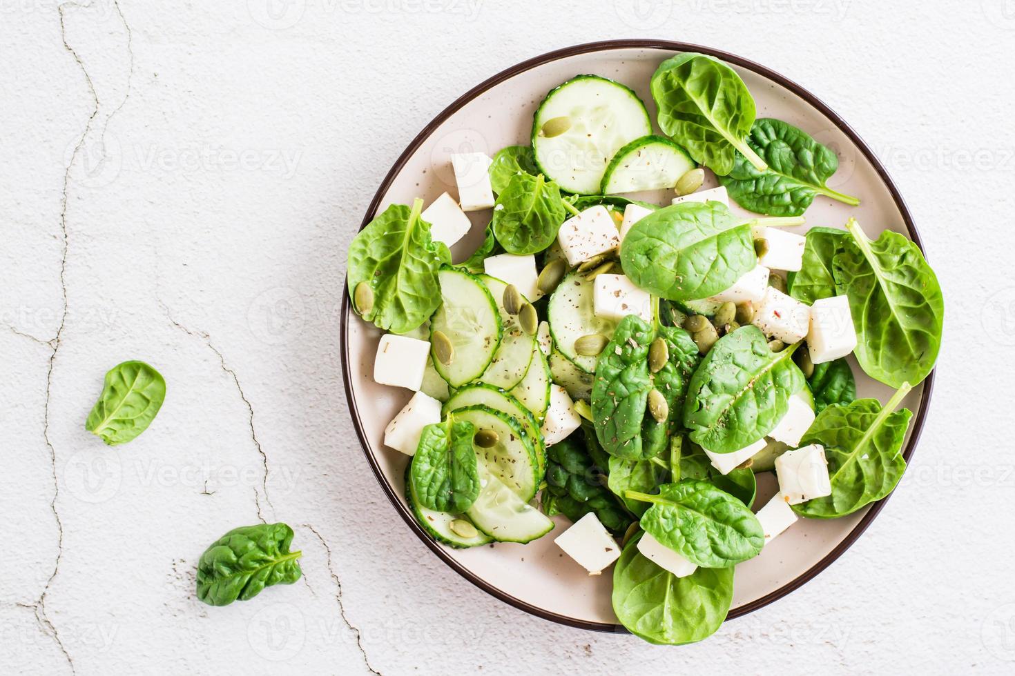 Fresh salad of cucumbers, spinach, cheese and pumpkin seeds in a plate. Top view. Close-up photo