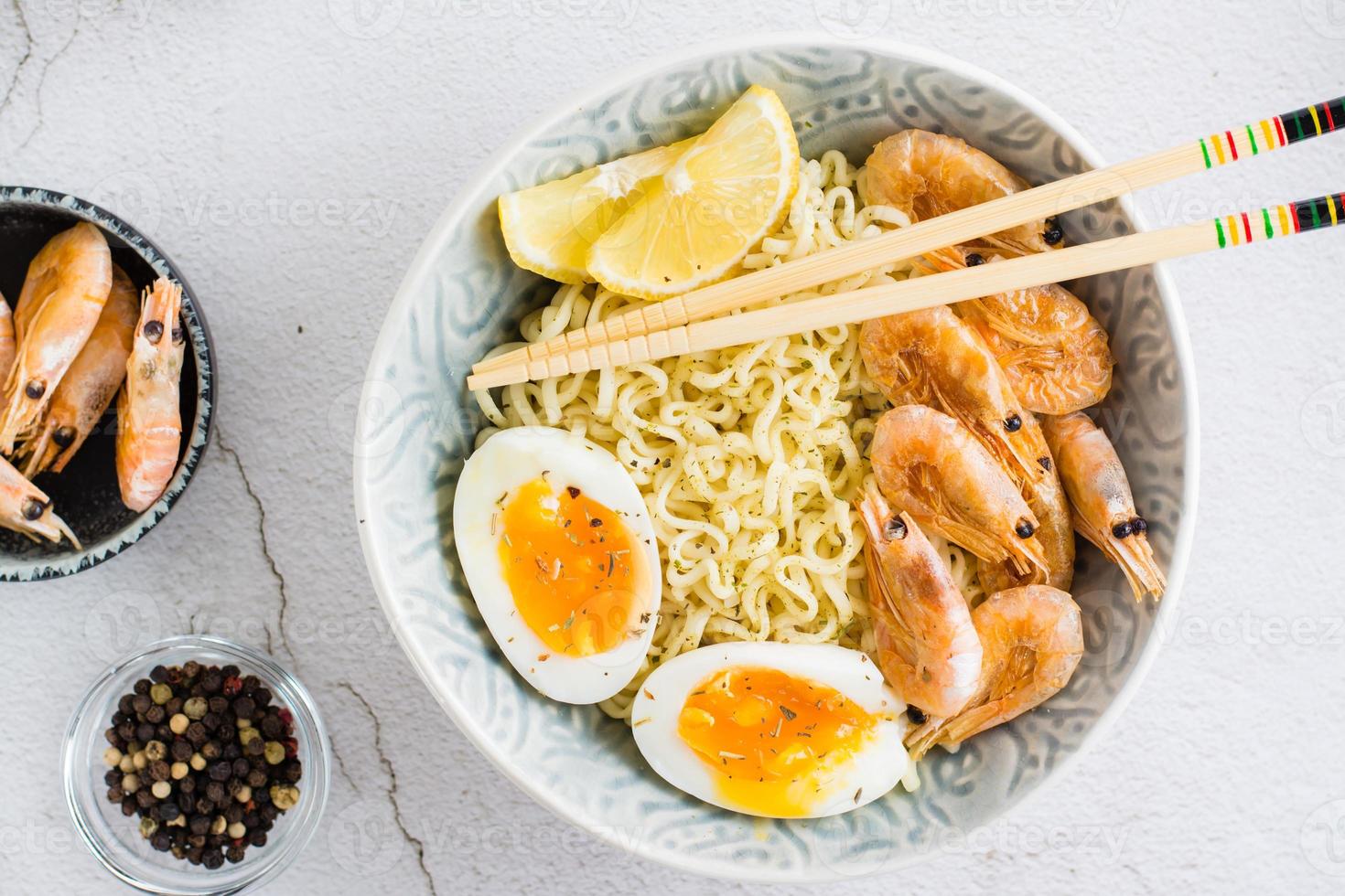 Chinese noodles with fried shrimp, boiled egg and lemon and chopsticks in a bowl. Top view photo