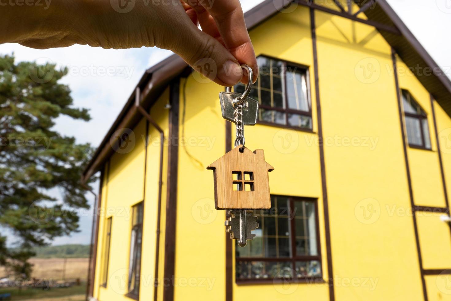 A hand with the keys to a new house on the background of an unfinished cottage. Building, project, moving to a new home, mortgage, rent and purchase real estate. To open the door. Copy space photo