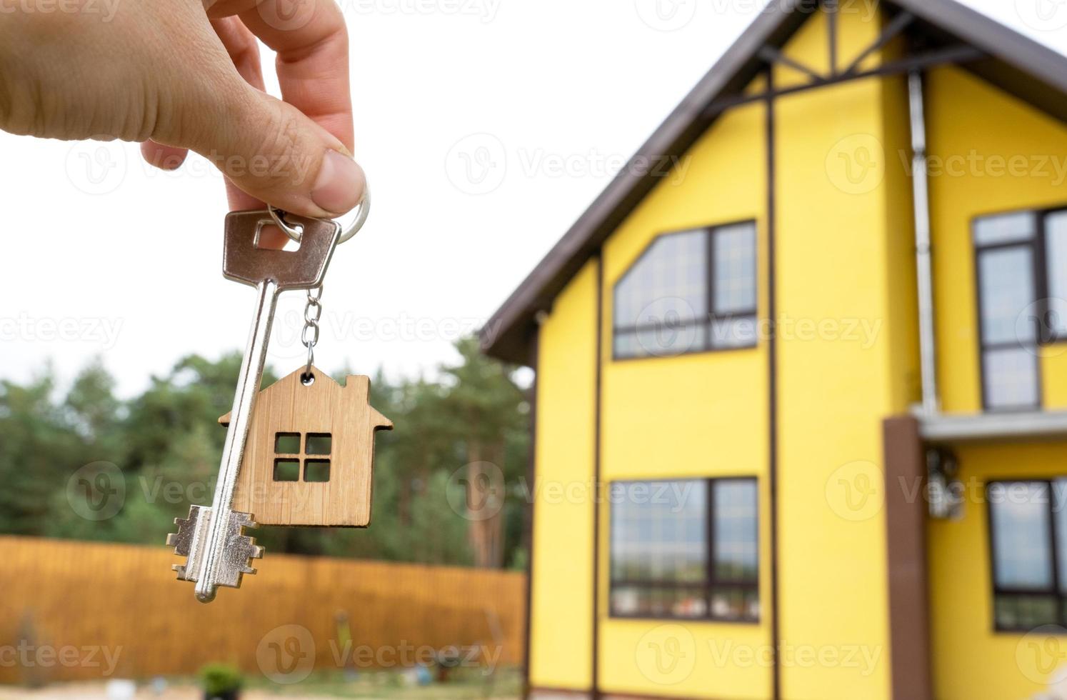 A hand with the keys to a new house on the background of an unfinished cottage. Building, project, moving to a new home, mortgage, rent and purchase real estate. To open the door. Copy space photo