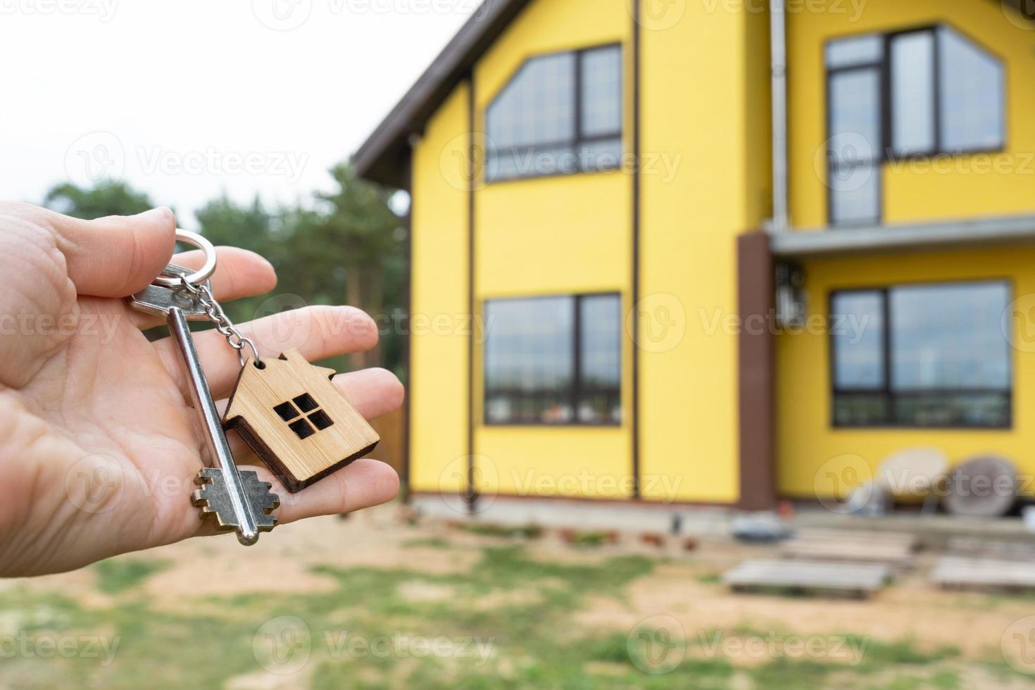 A hand with the keys to a new house on the background of an unfinished cottage. Building, project, moving to a new home, mortgage, rent and purchase real estate. To open the door. Copy space photo