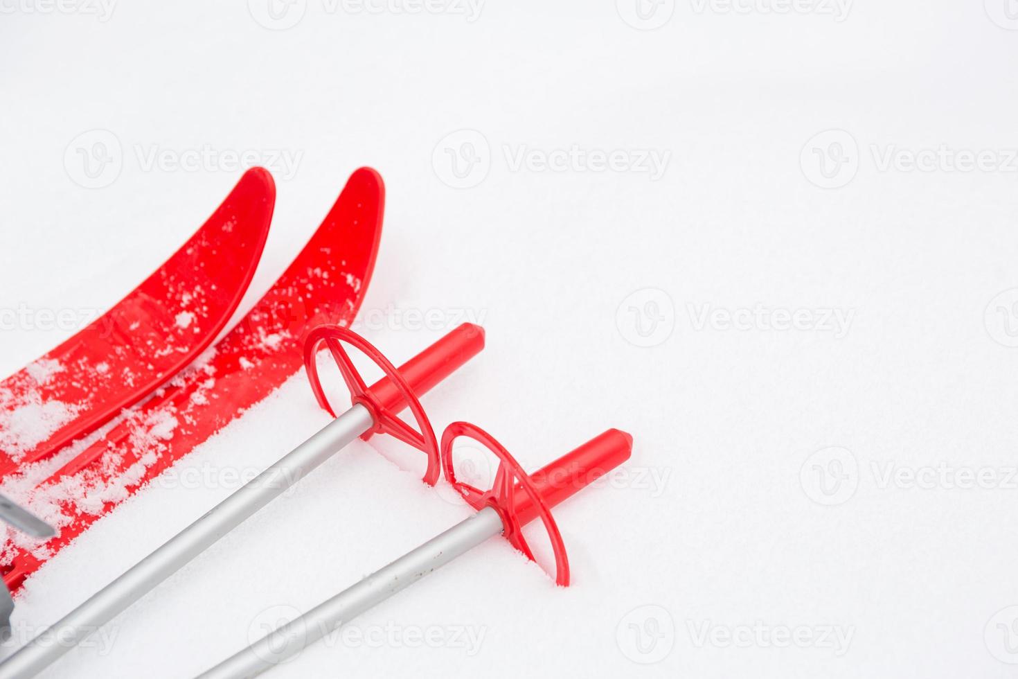 esquís rojos para niños con palos -disposición en la nieve. deporte de invierno para niños, actividades al aire libre, diversión familiar. fondo escarchado natural blanco. copie el espacio foto