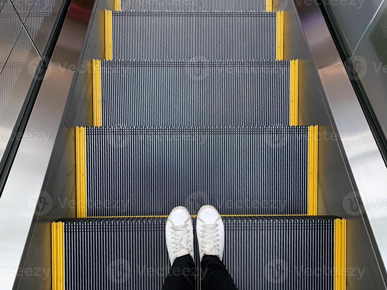 Selfie of feet in white sneakers shoes standing on escalator in shopping mall or modern office photo