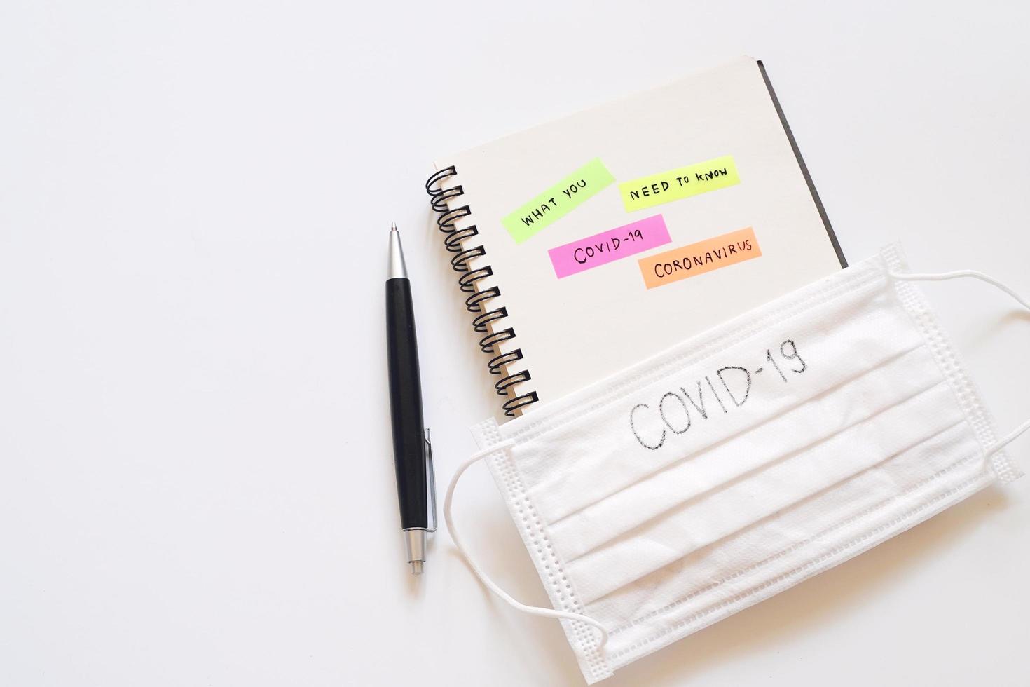 Flat lay of word What you need to know about Covid-19 with Coronavirus text written on post it with notebook and copy space, surgical mask with covit-19 text, global pandemic risk concept photo