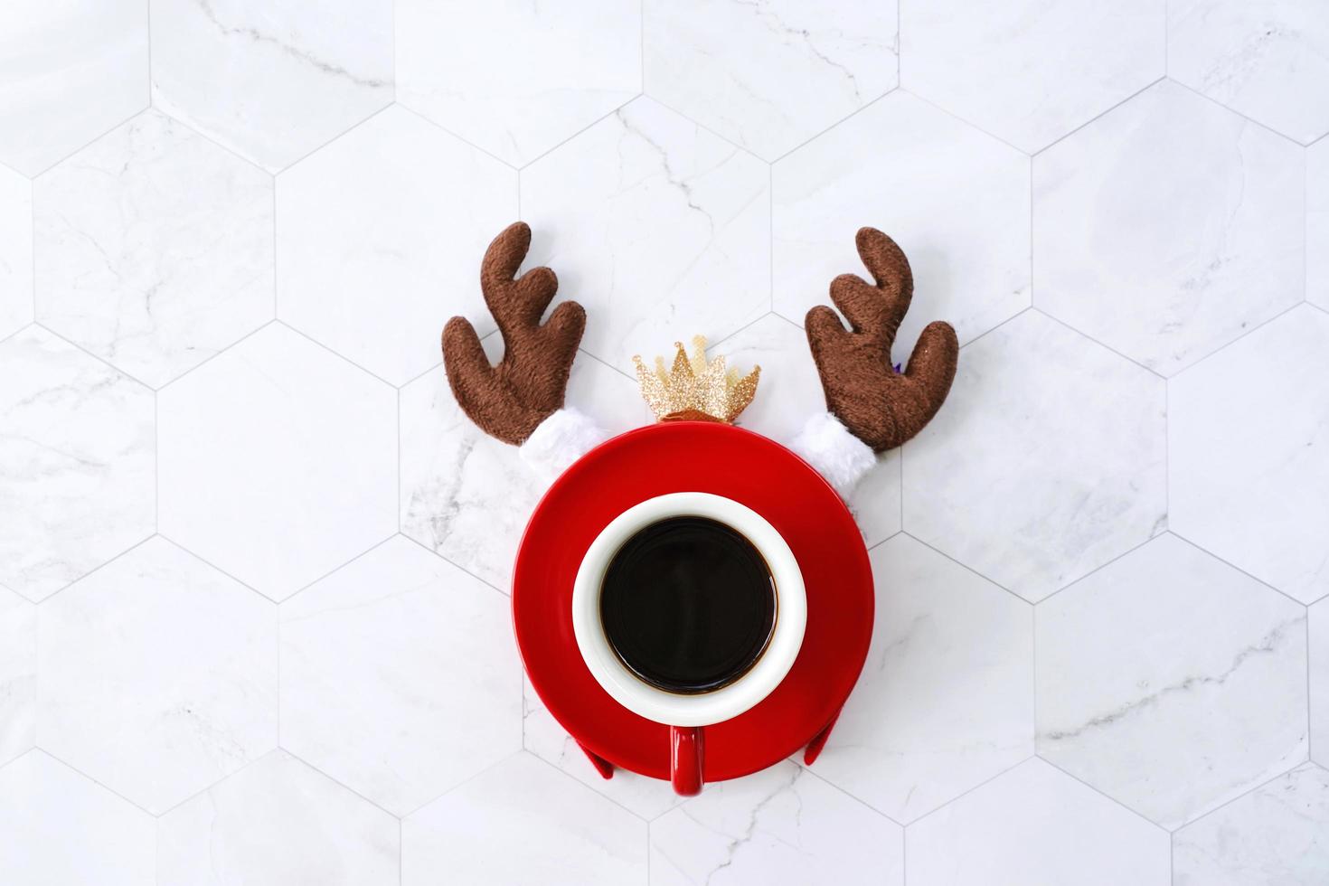 Flat lay of black coffee red cup with reindeer headband for christmas celebration on white marble background, holiday concept photo