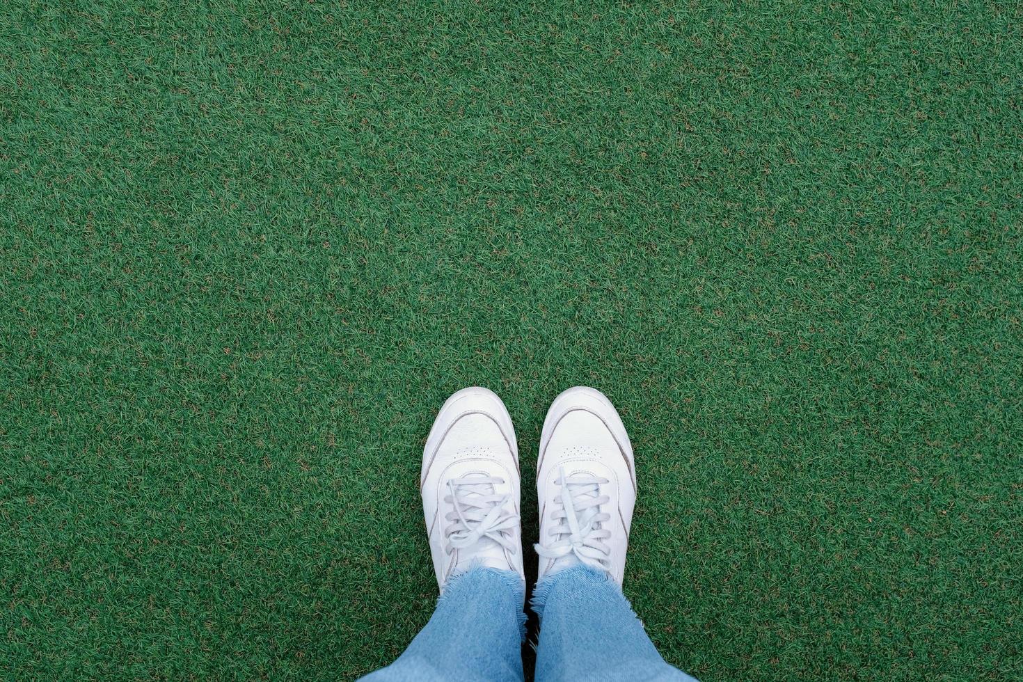 Selfie of feet in white sneakers shoes on green grass background with copy space, spring and summer with fashion lifestyle concept photo