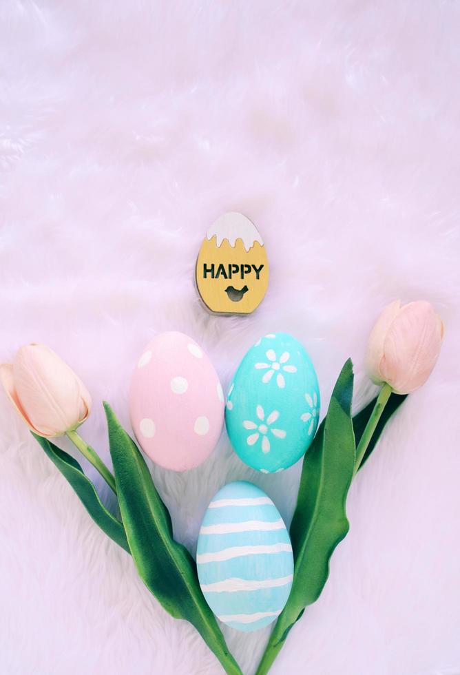 Happy Easter holiday concept with colorful easter eggs on white fur background and pink tulips. Top view with copy space photo