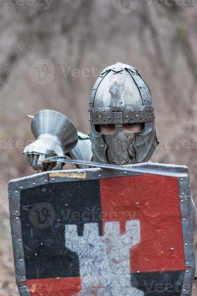 noble guerrero. retrato de un guerrero medieval o caballero con armadura y casco con escudo y espada posando foto