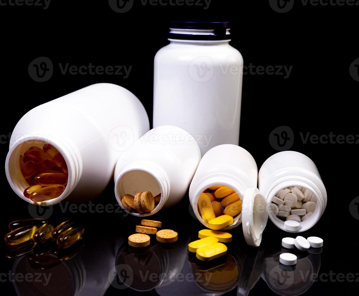 Medical pills flow from a white jar on an isolated black background with reflection photo