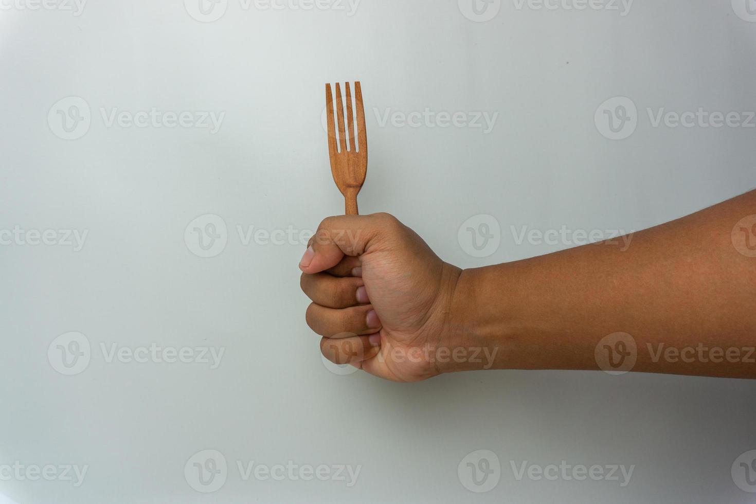 Mano sujetando cuchara y tenedor de madera aislado sobre fondo blanco. foto