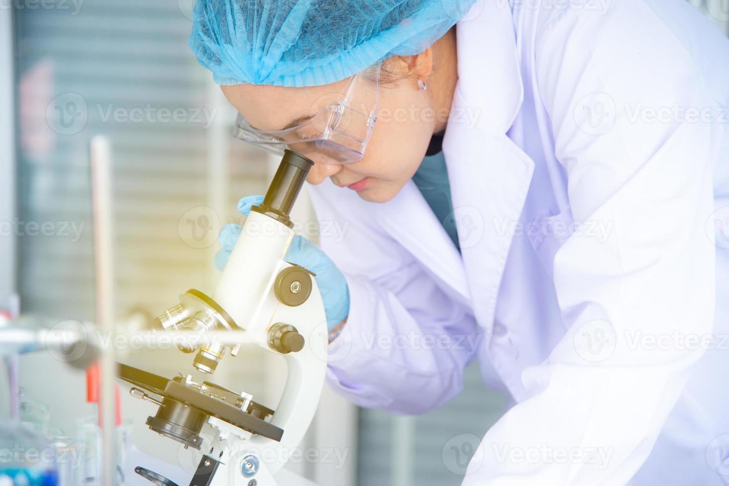 Asian woman scientist, researcher, technician, or student conducted research or experiment by using microscope which is scientific equipment in medical, chemistry or  biology laboratory photo