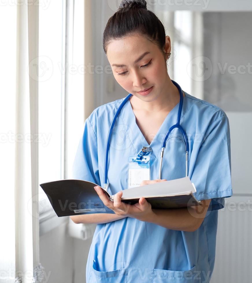 mujer médico persona usa uniforme y estetoscopio leyendo documento de información del paciente para consulta de cirugía. enfermera profesional asiática está trabajando como consulta de atención médica en el hospital foto