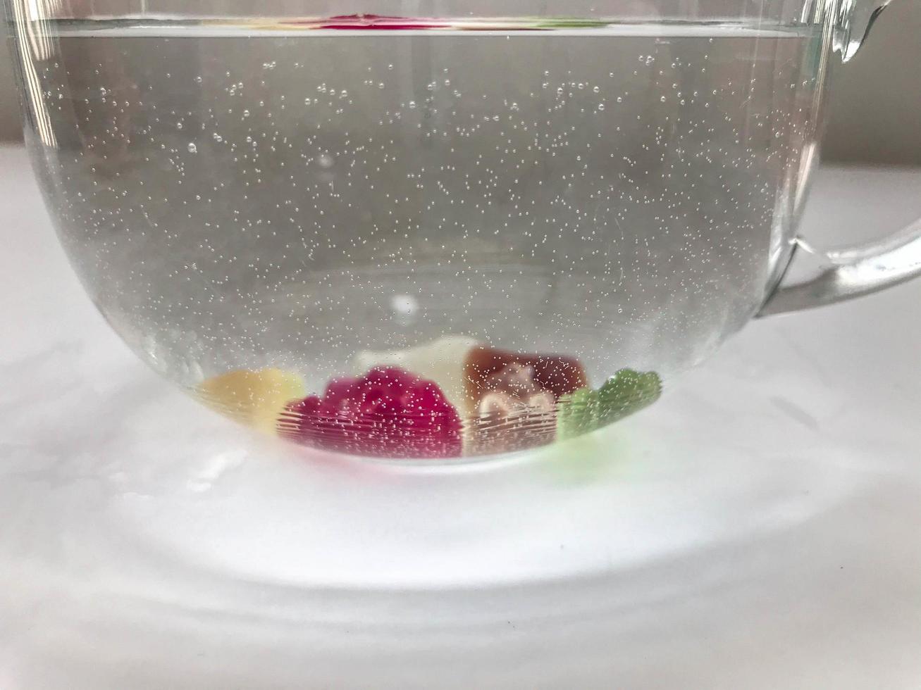 transparent mug, round and large, filled with water. at the bottom of the mug are gummy bears. reflection of bears in water, voluminous and inhomogeneous sweets photo