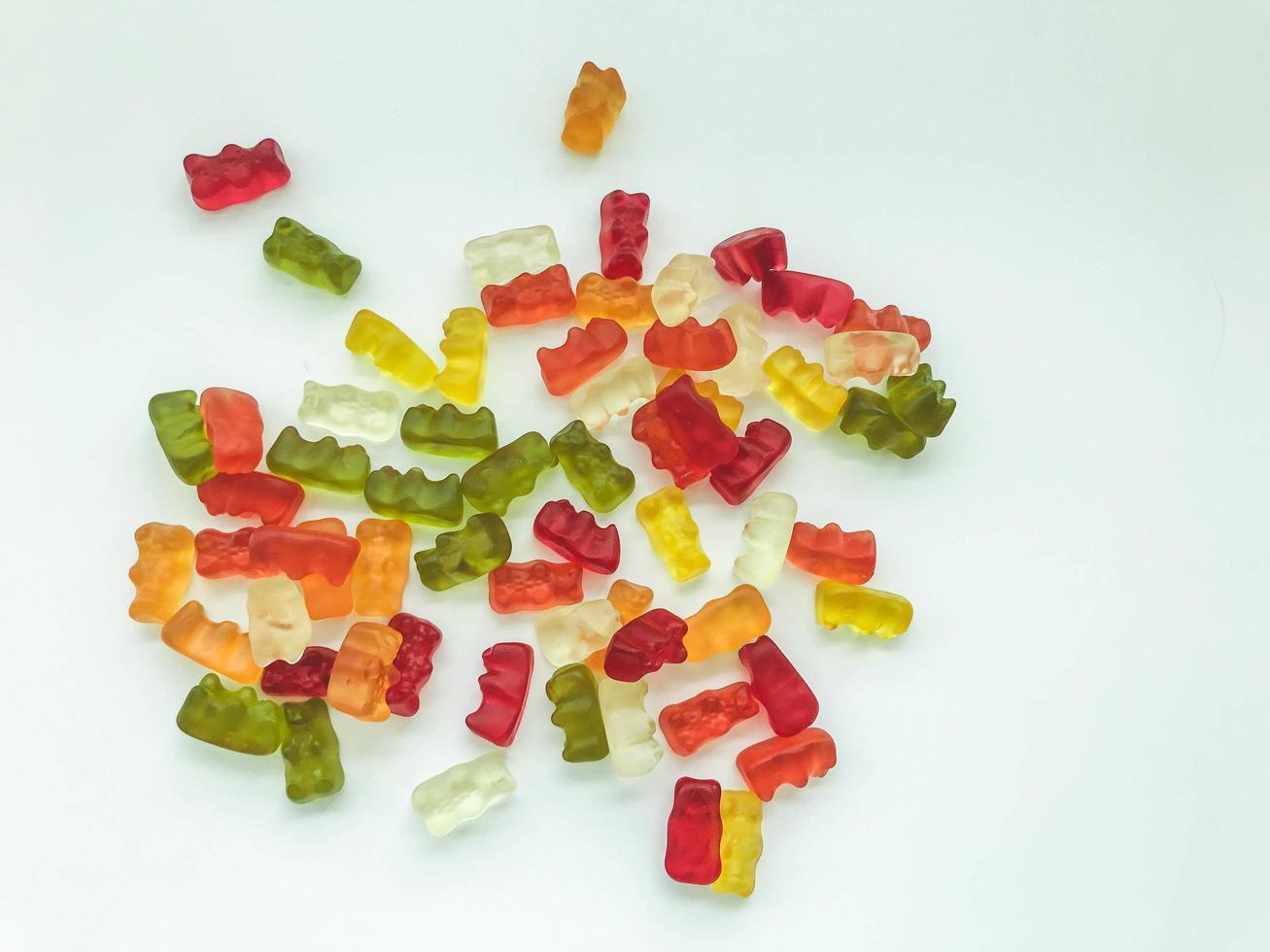 gummy bears of different colors lie on a matte white background. delicious variety of sweets. gelatinous gummies desired. delicious bears, edible sweet dessert photo