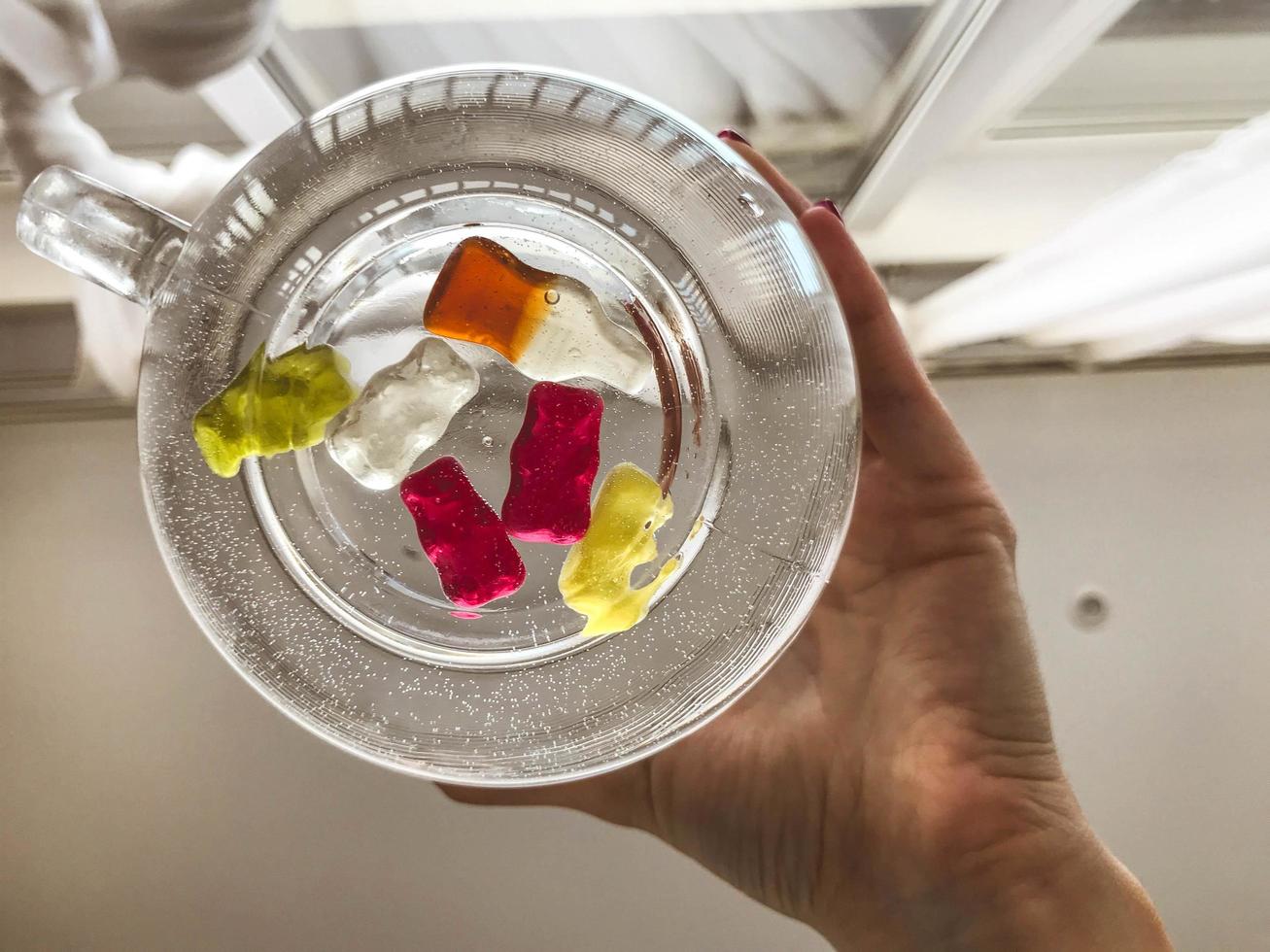 Bright tasty beautiful juicy multi-colored gelatinous gummy sweet candies bear cubs lie in a glass mug with a woman's hand. Sweet dessert cocktail photo