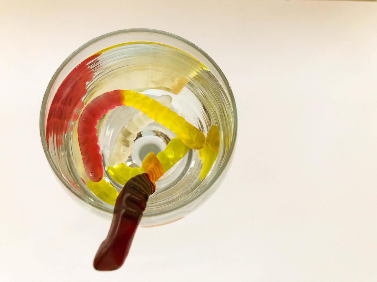gummy worms in a transparent glass with water. bright, sweet gummy worms drown in water. red-yellow, brown-yellow worms float in water. game of gummy worms photo
