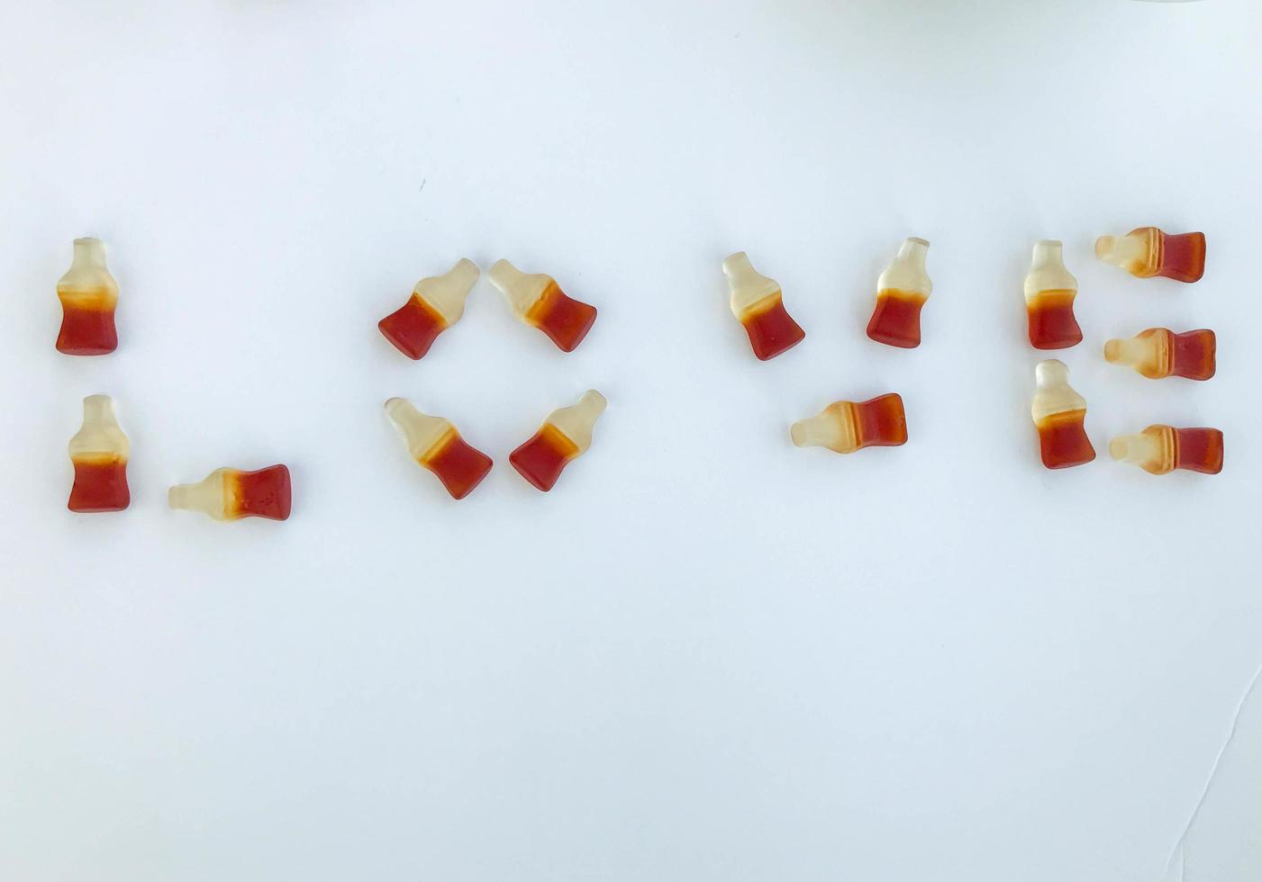 the word love is laid out on a white matte marmalade background. gelatin candy in the form of bottles with lemonade. sweet appetizing dessert. creative lettering photo