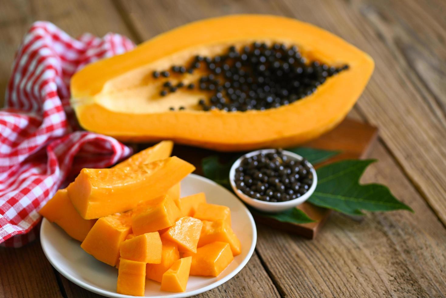 frutas de papaya sobre fondo de madera, rodajas de papaya maduras frescas sobre un plato blanco fruta tropical con semillas de papaya y hojas de árbol de papaya foto