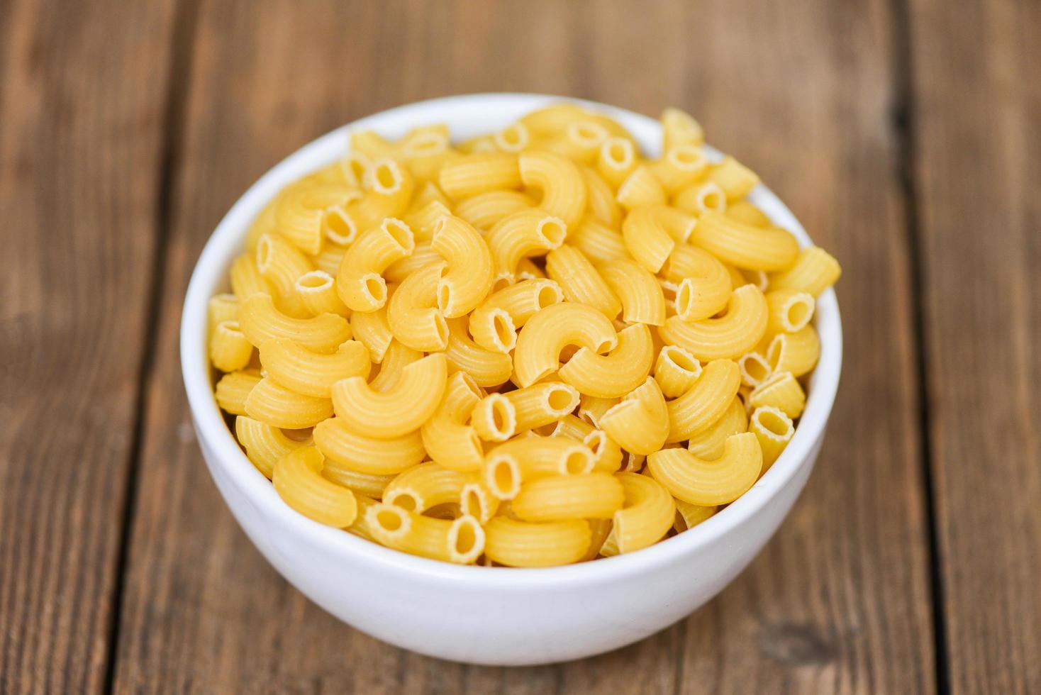 macaroni top view on bowl and wooden background - close up raw macaroni uncooked delicious pasta or penne noodles photo