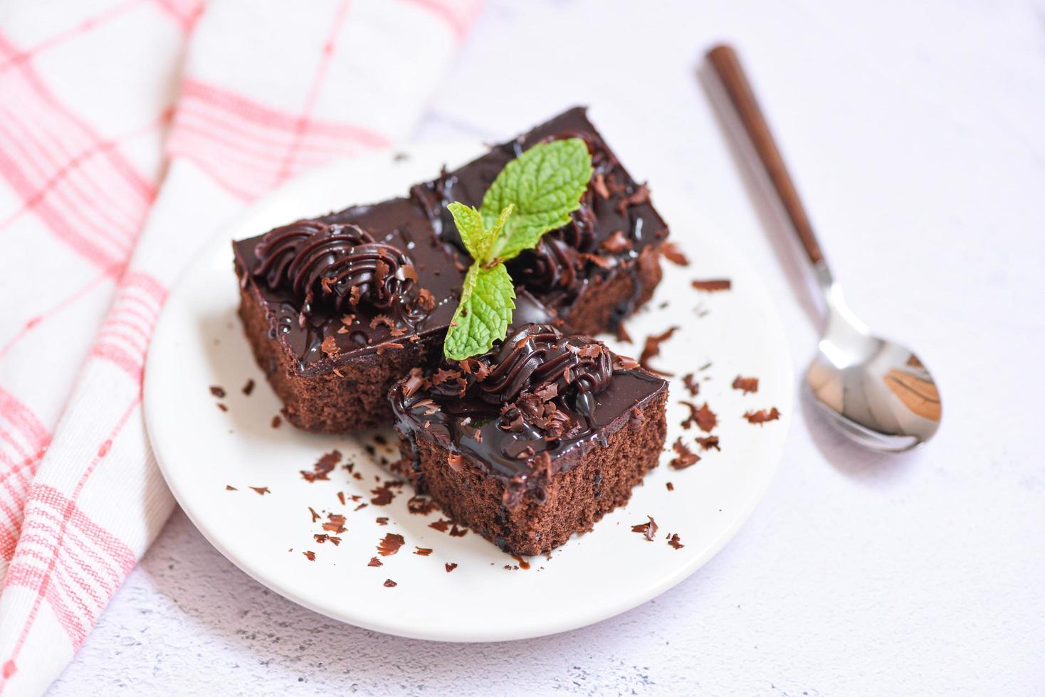 Pastel de chocolate delicioso postre servido en la mesa - rebanada de pastel en un plato blanco con cobertura de chocolate y hojas de menta foto