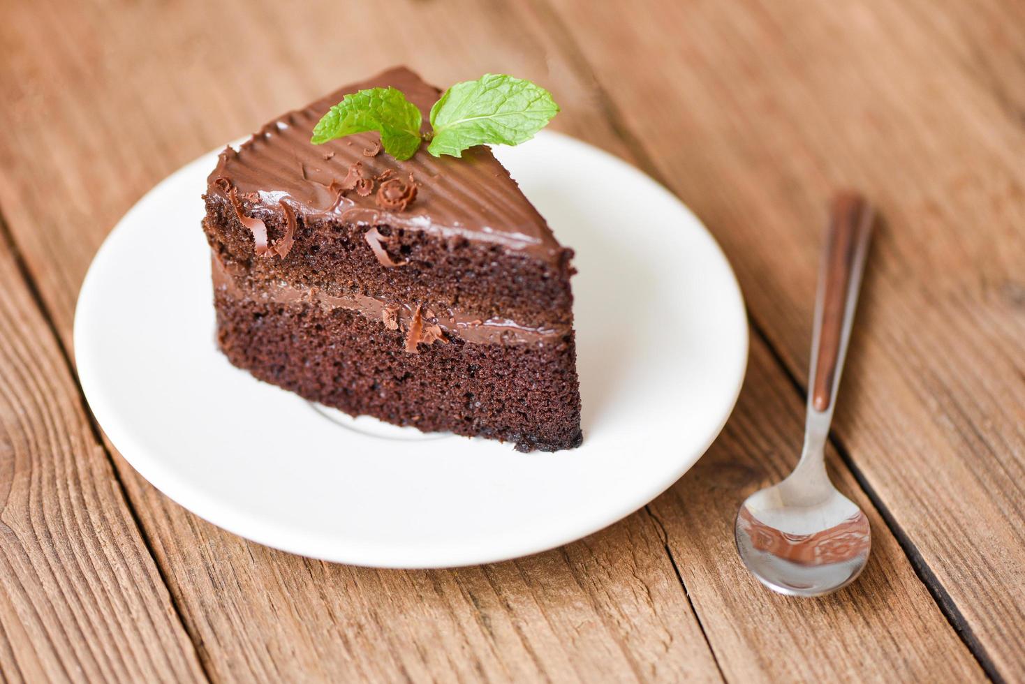 Cake chocolate delicious dessert served on the wooden table - cake slice on white plate with topping chocolate and mint leaf photo