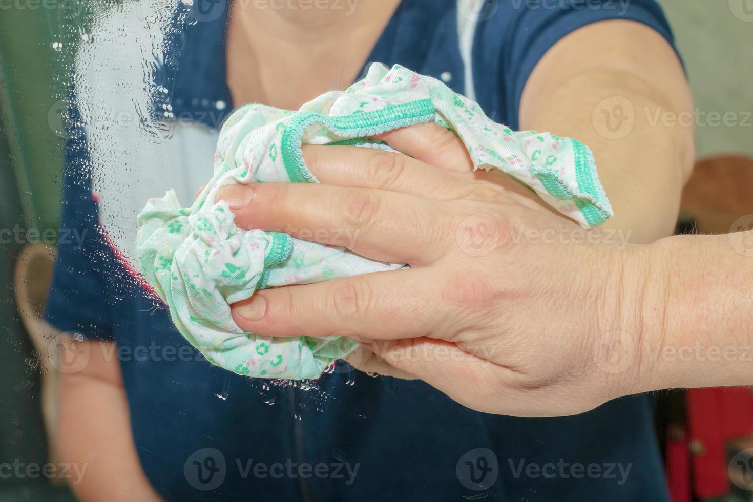 A woman cleans a mirror with a napkin from dirt and plaque from water at home photo