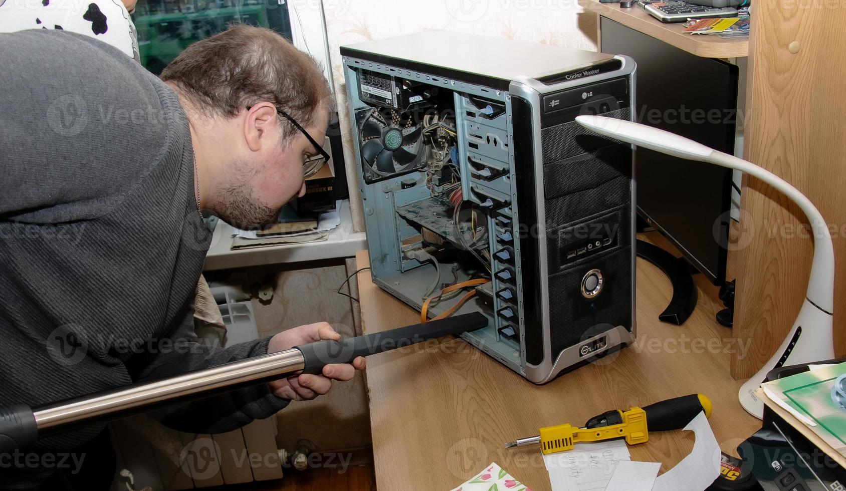 el programador limpia la unidad del sistema informático de escritorio del polvo con una aspiradora. foto