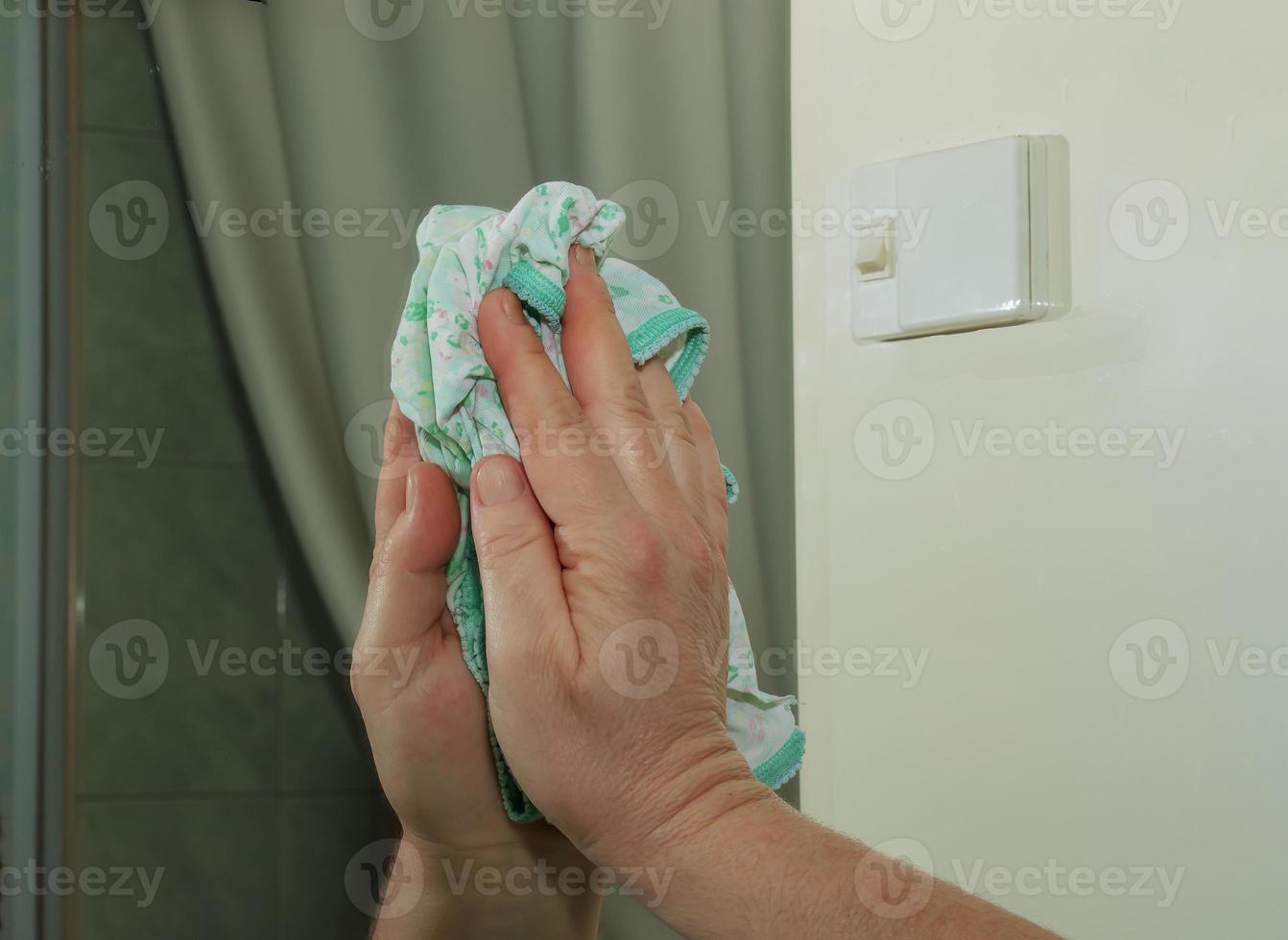 A woman cleans a mirror with a napkin from dirt and plaque from water at home photo