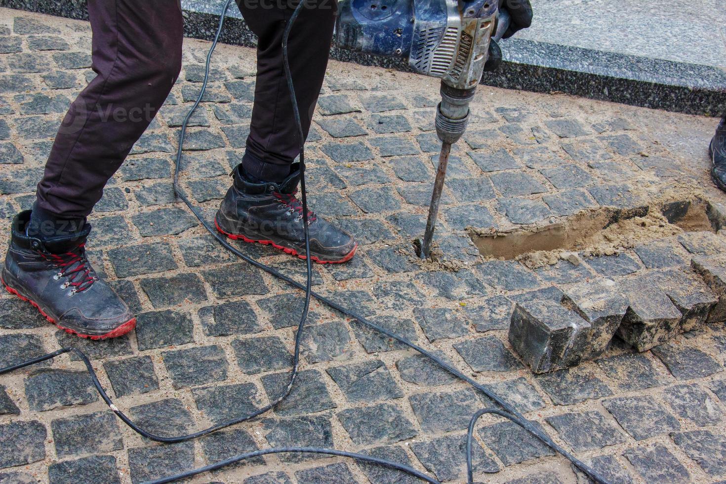 A male worker repairs the pavement with a jackhammer. The work of the municipal service photo