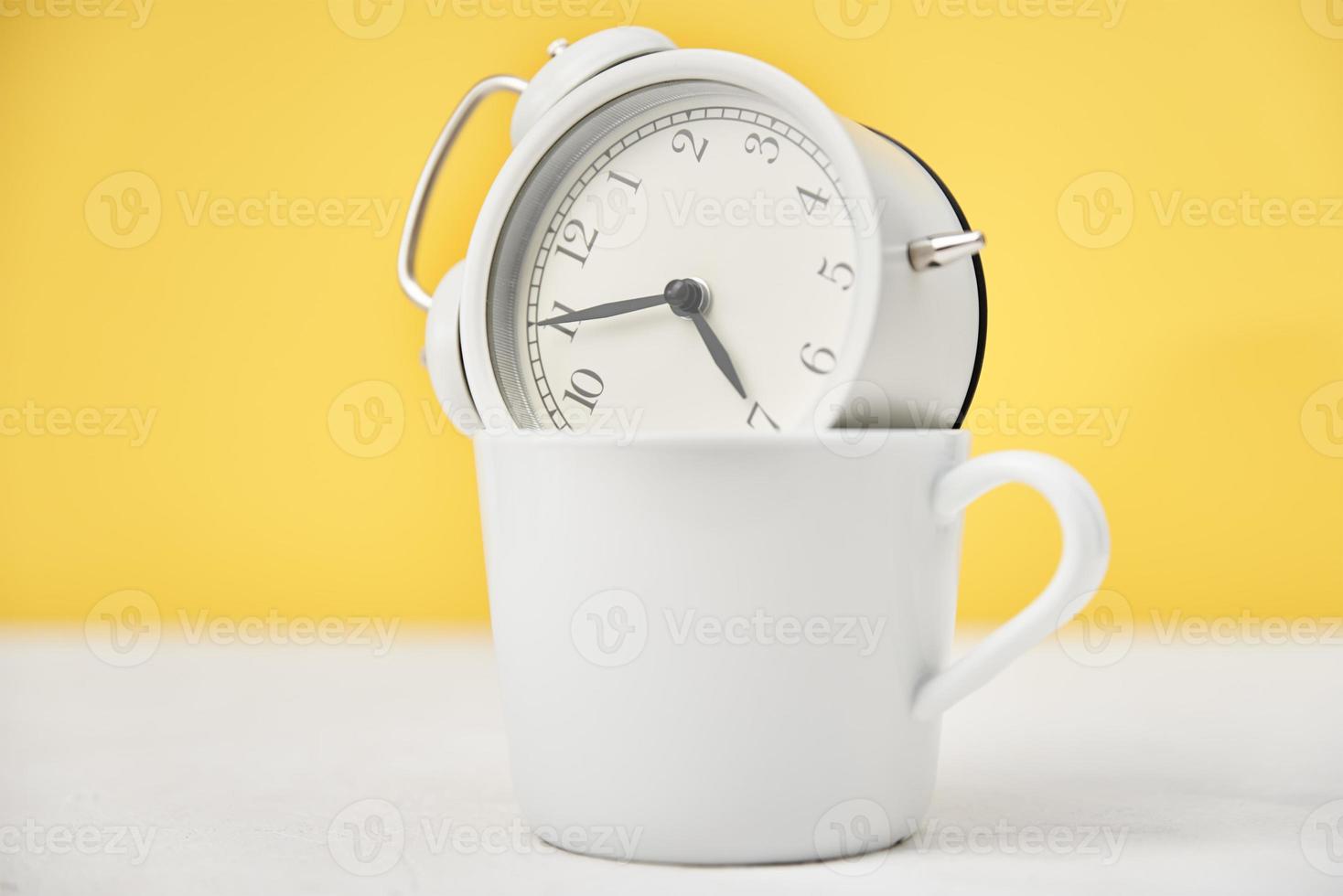 White retro alarm clock in cup on yellow background. Morning time concept photo