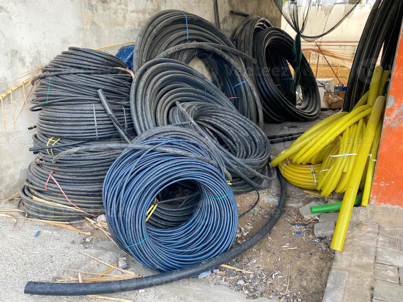 Many large coils of black cables in plastic insulation or electrical wires for electricity in an industrial warehouse photo