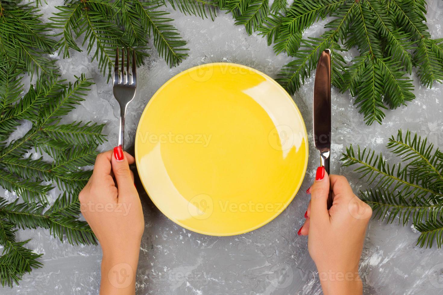 Hungry woman waiting for meal. empty yellow plate on a gray background with Christmas branches. view from above for your design photo
