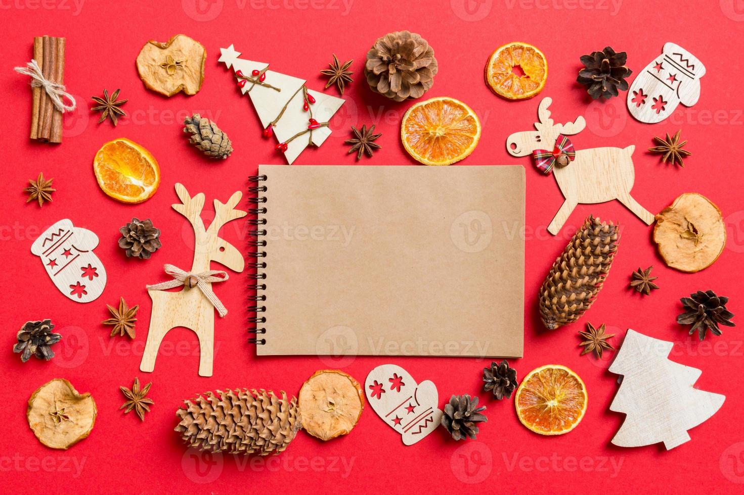 Top view of notebook, red background decorated with festive toys and Christmas symbols reindeers and New Year trees. Holiday concept photo