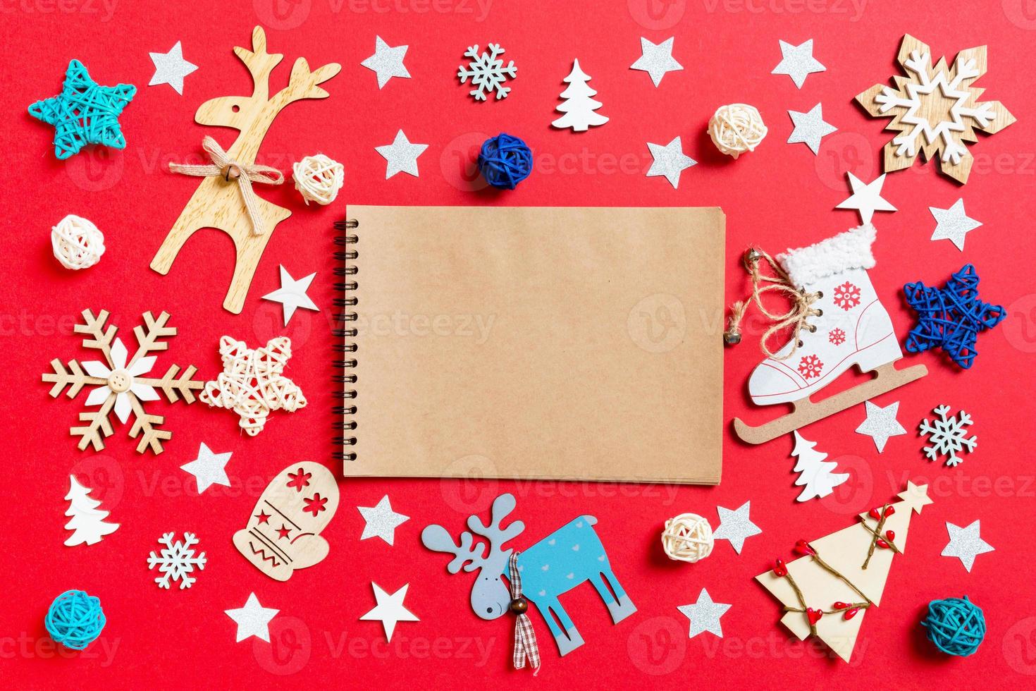 Top view of notebook, holiday toys and decorations on red Christmas background. New Year time concept photo