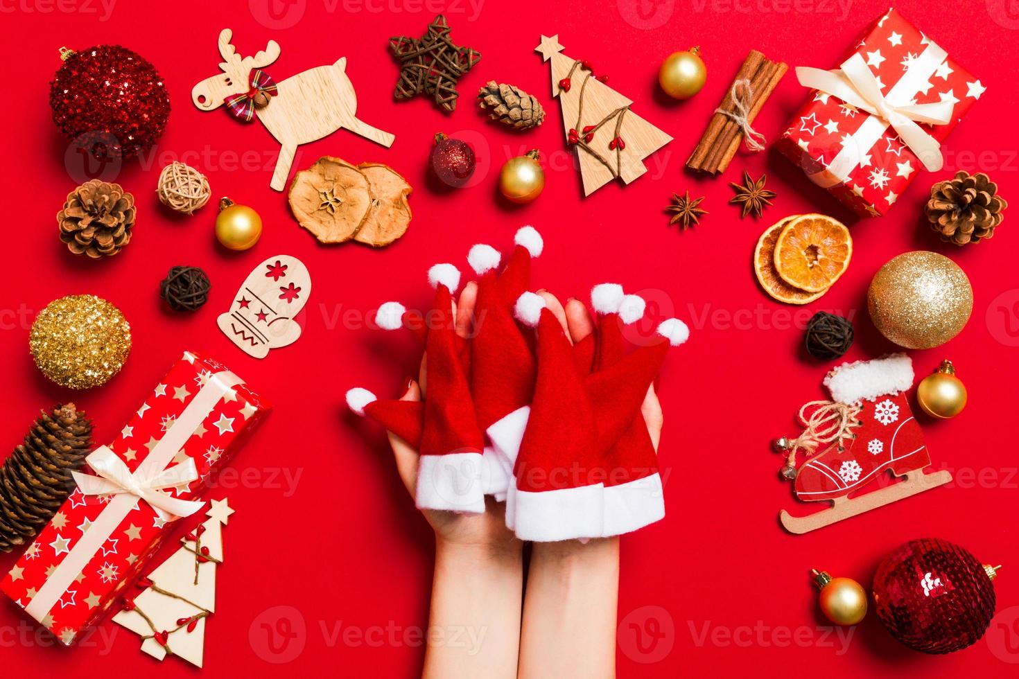 Top view of female hands holding a stack of santa hats on red background. New year decorations. Christmas holiday concept photo