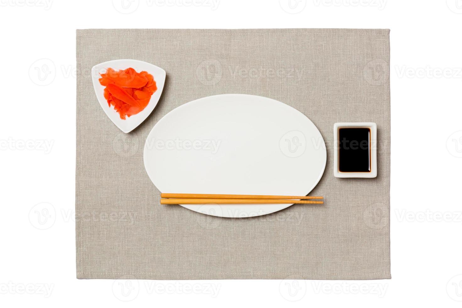 Empty oval white plate with chopsticks for sushi, ginger and soy sauce on grey napkin background. Top view with copy space for you design photo