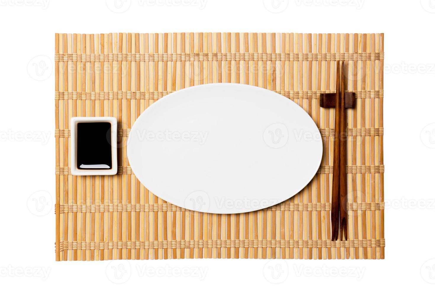 Empty oval white plate with chopsticks for sushi and soy sauce on yellow bamboo mat background. Top view with copy space for you design photo