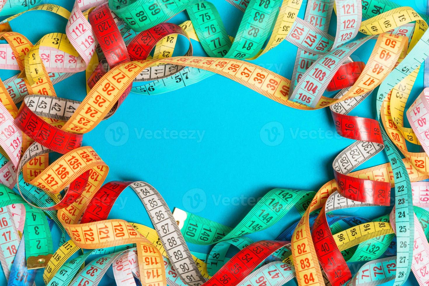 Top view of frame made of heap of colorful measure tapes on turquoise background. Keeping fit concept with empty space for your design photo