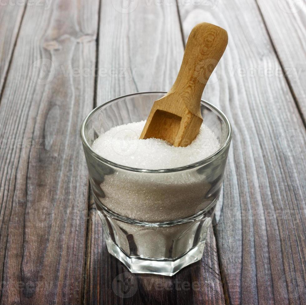 azúcar granulada blanca en taza blanca con cuchara de madera sobre fondo de madera oscura foto