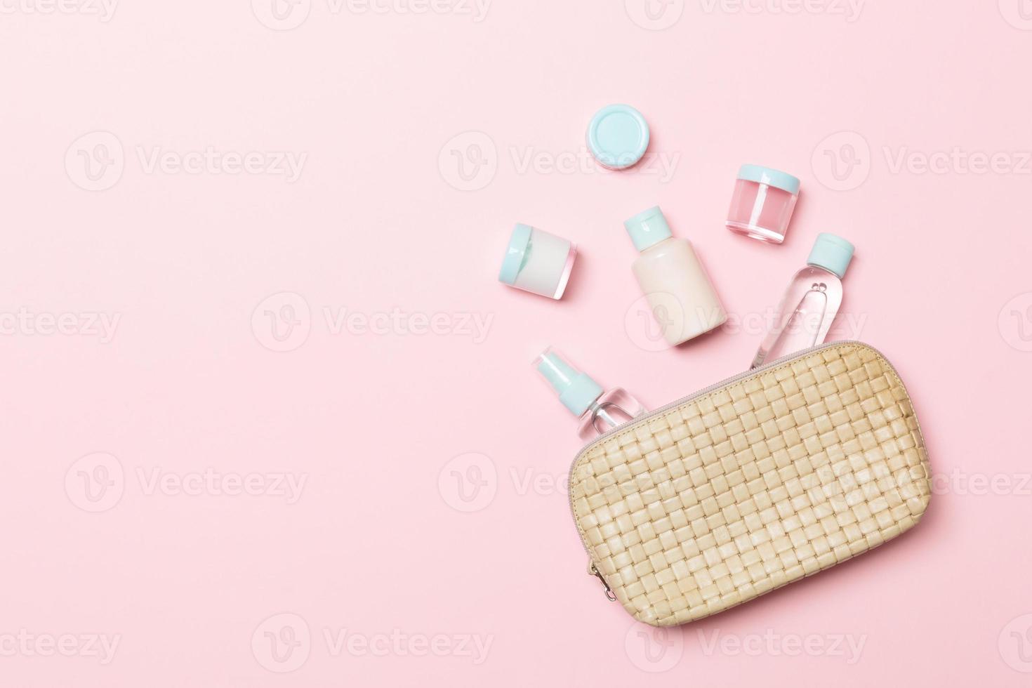 Group of beauty cream bottles dropped out of the cosmetics bag on pink background. Space for your design. Top view of skincare concept photo